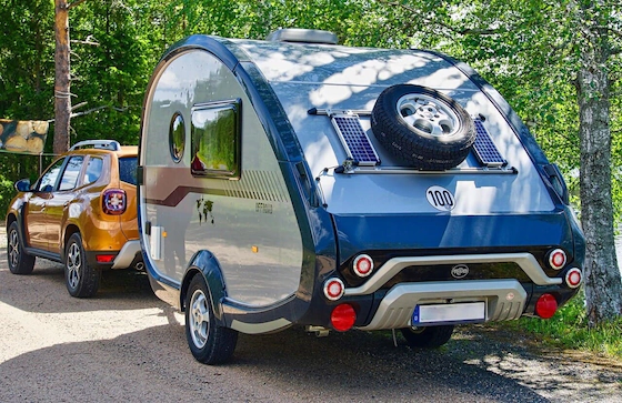 прицеп-кемпер с солнечными панелями и запасным колесом на стоянке в лесу